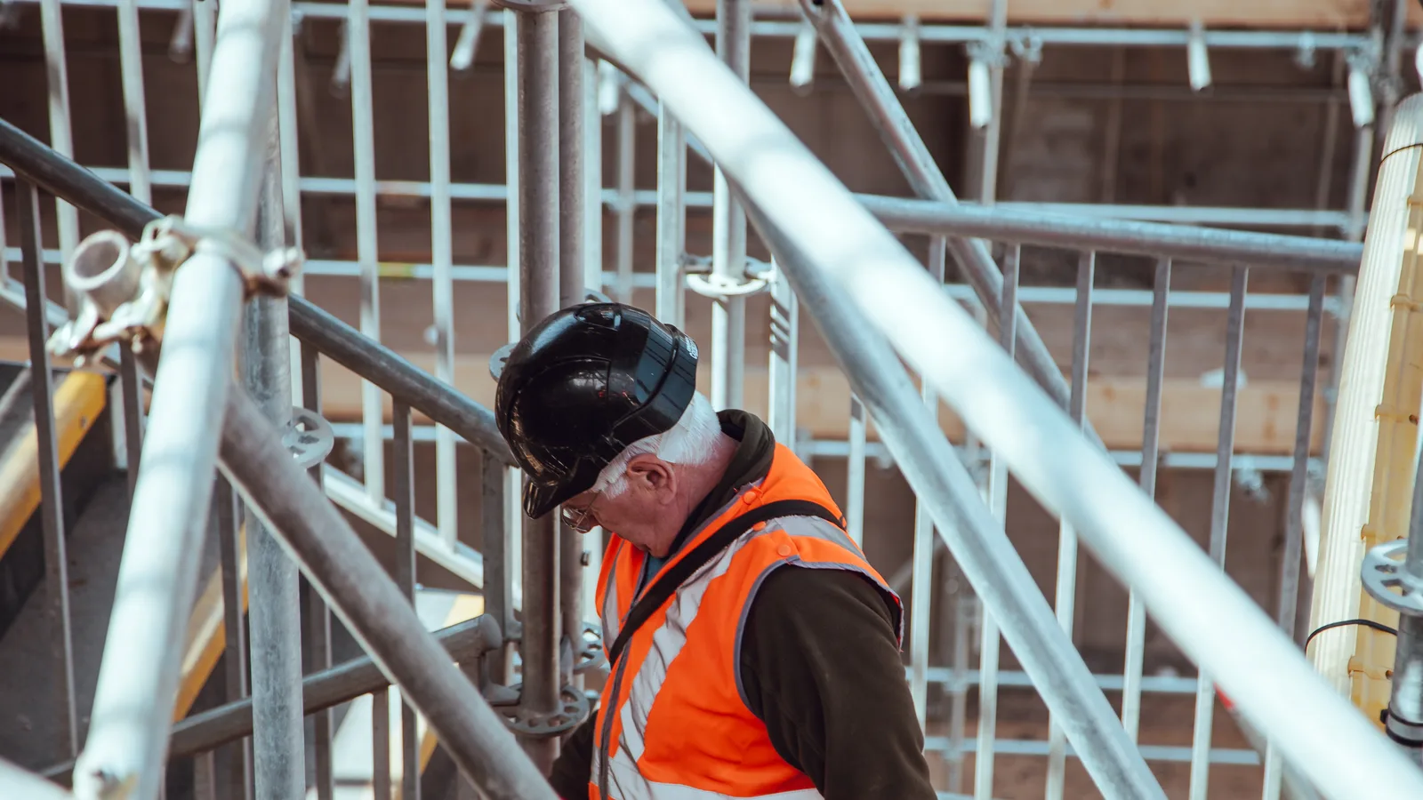 A construction worker in a hard hat and high-visibility vest on scaffolding