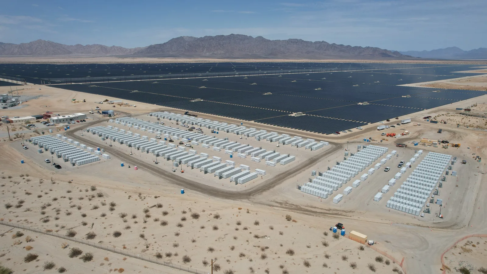 Solar arrays and battery storage units across a desert plain, seen from the air