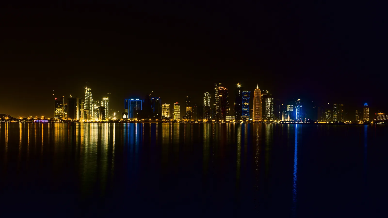 The Doha skyline lit at night, reflected in the bay