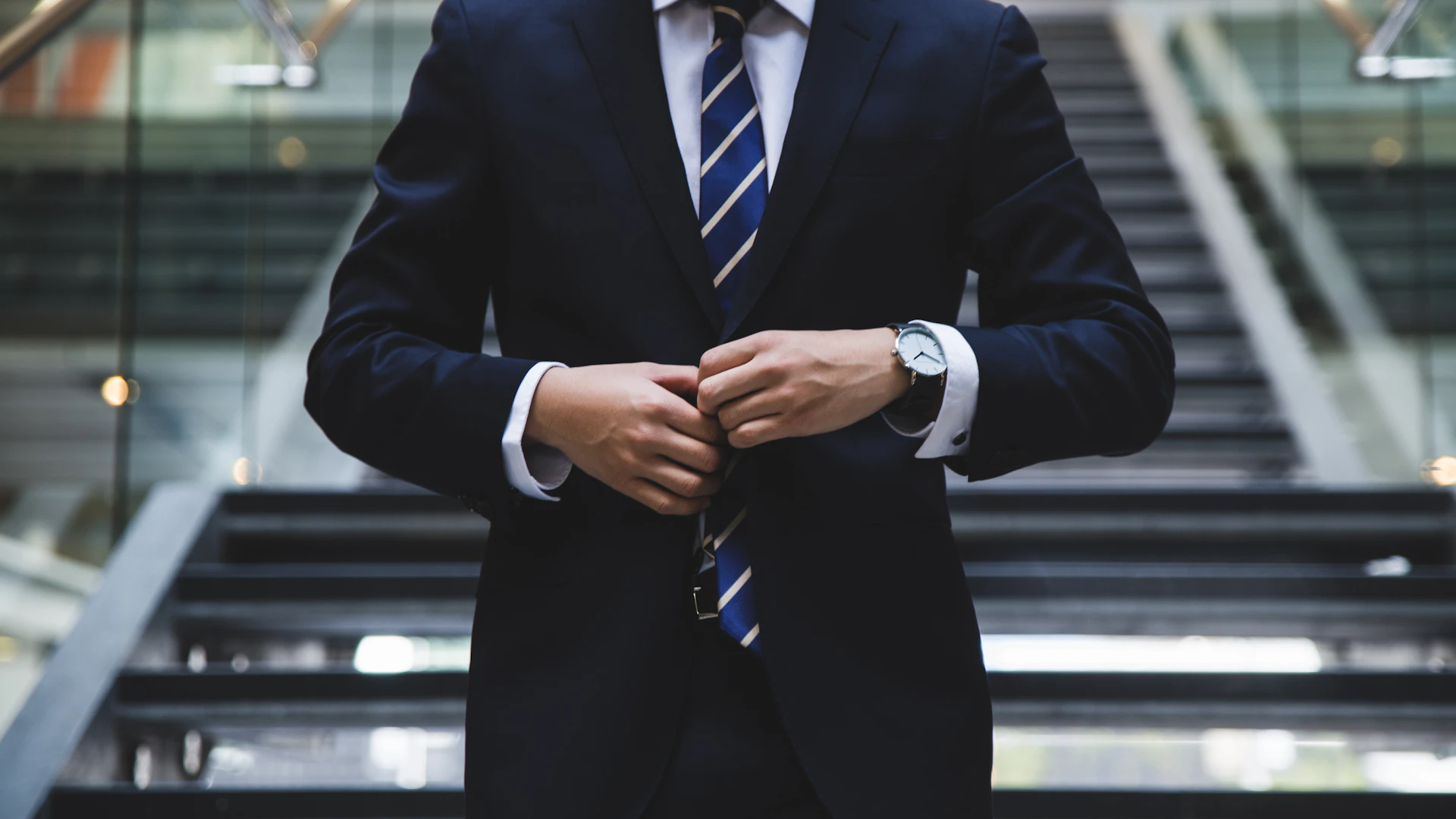 An executive in a navy suit at the foot of an office staircase
