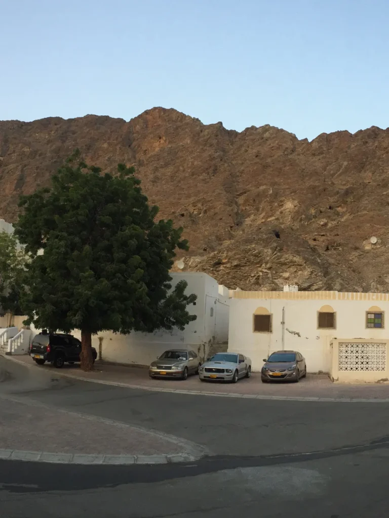 A rocky hill above white houses on a street in Muscat, Oman