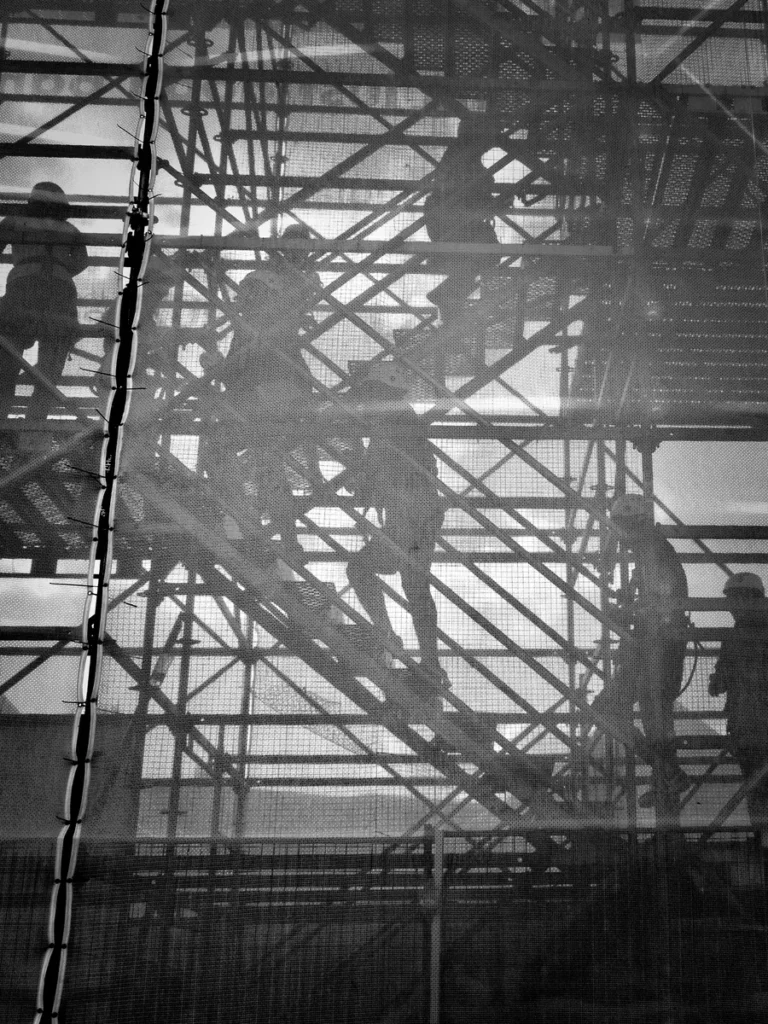 Workers silhouetted on scaffolding, in black and white