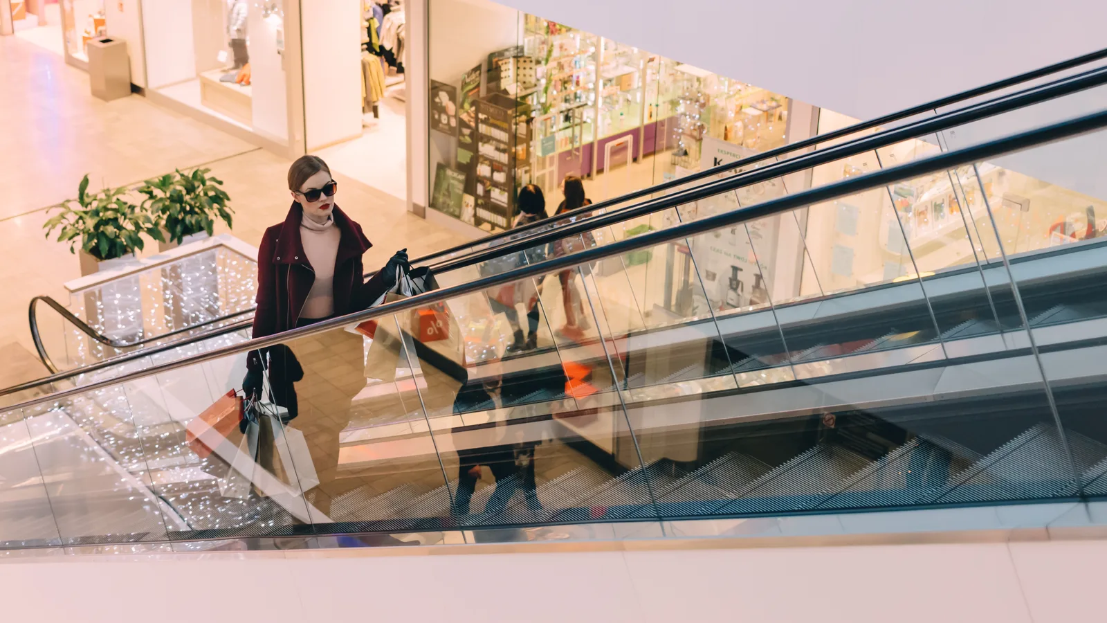 A shopper with bags riding an escalator in a shopping centre