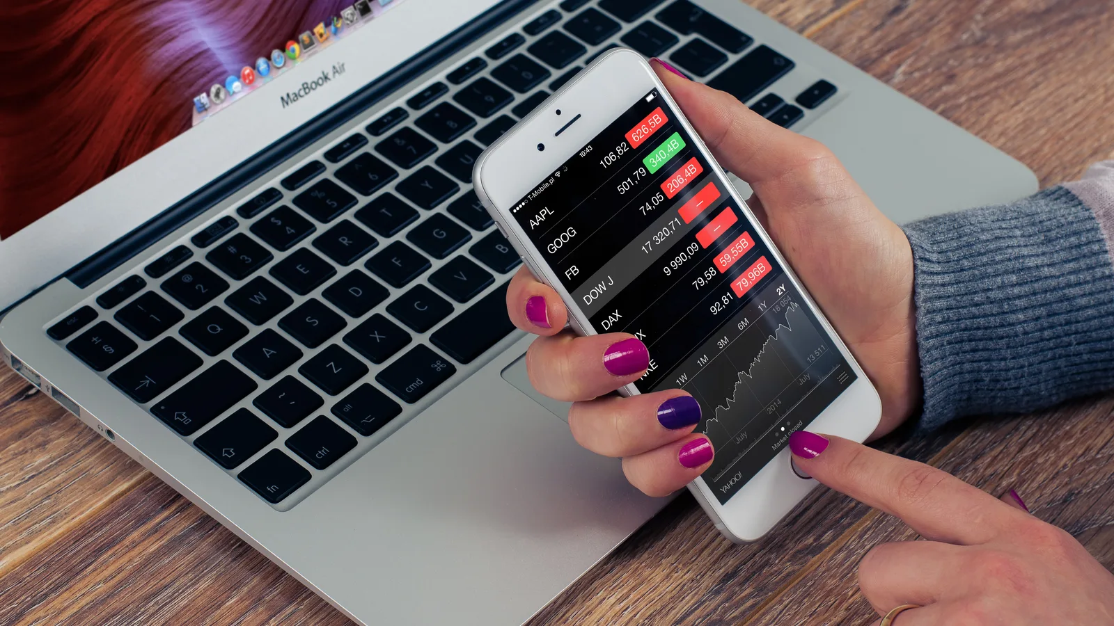 Checking stock market prices on a phone beside a laptop