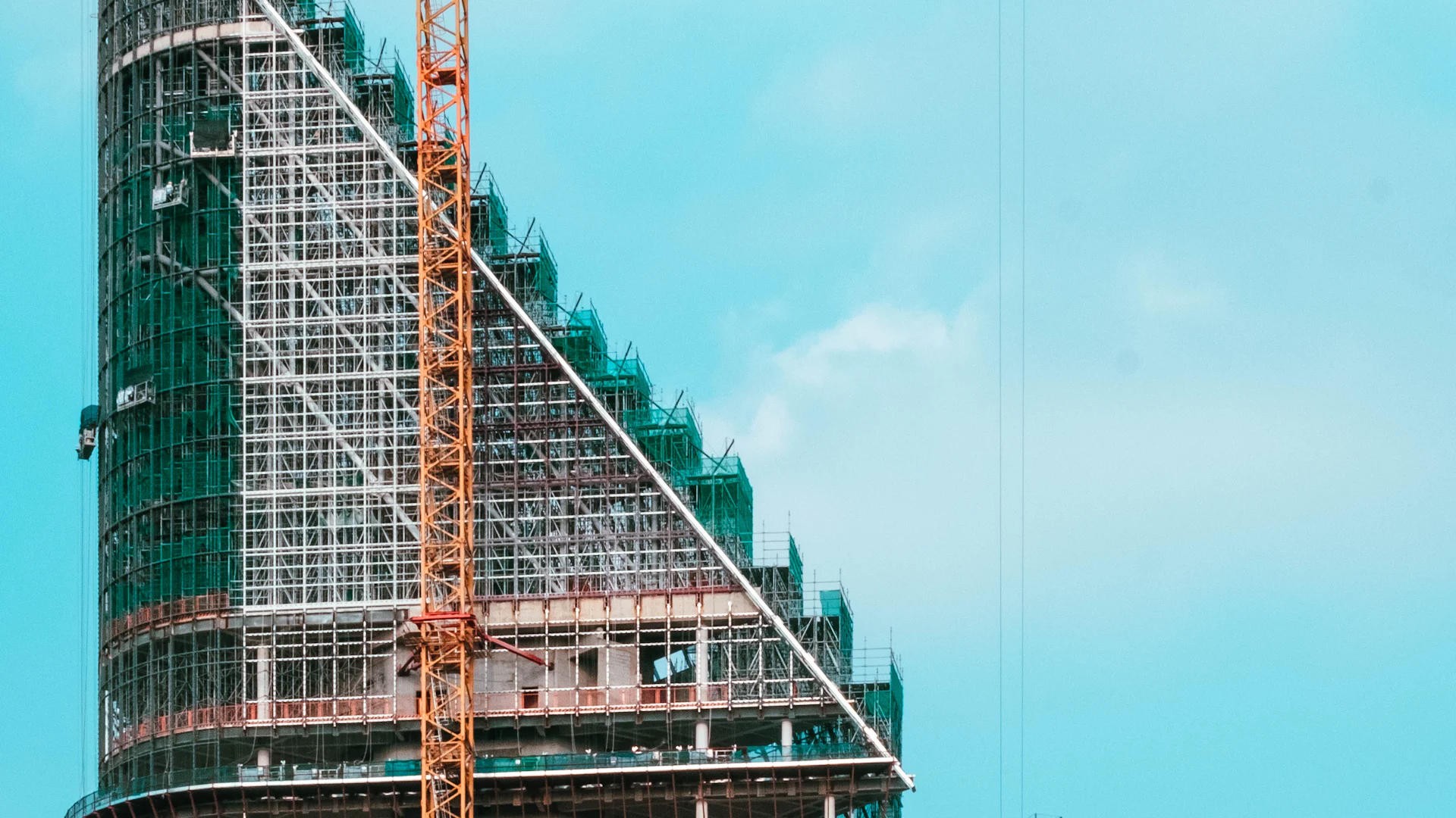 A glass tower under construction with a crane above it